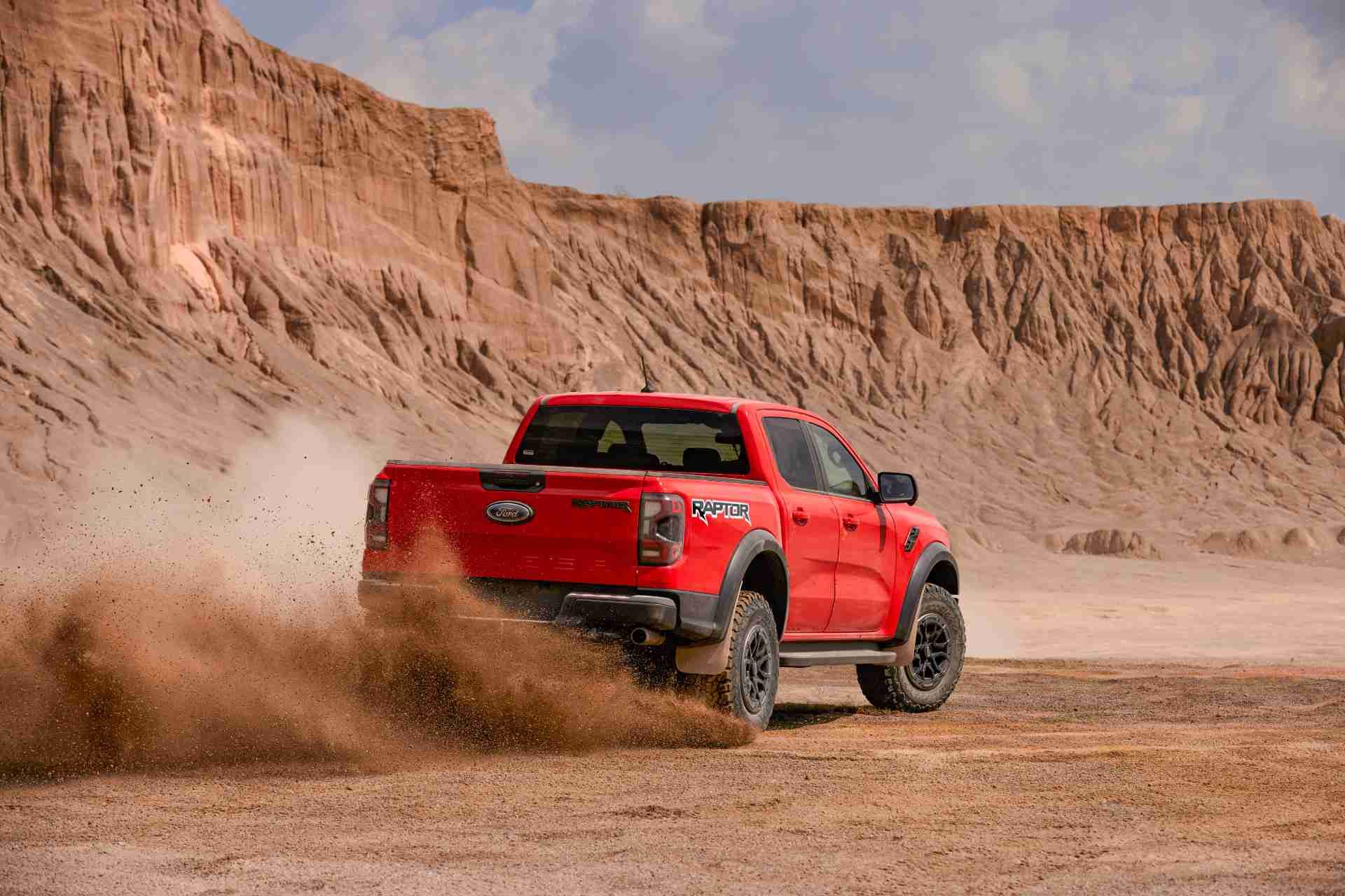 A red Ford Ranger Raptor driving on a sandy desert terrain, kicking up dust