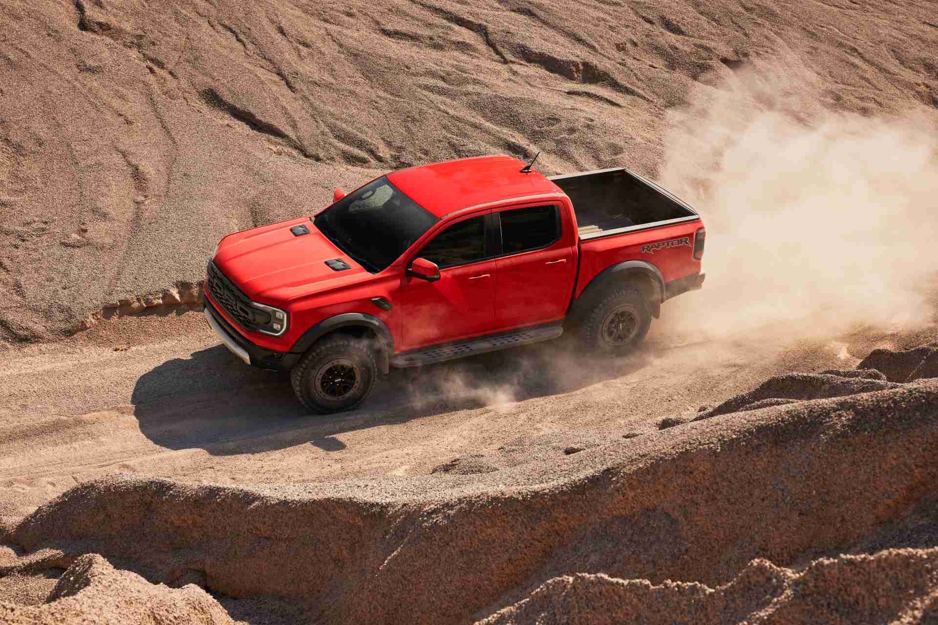 Ford Ranger Raptor driving through a sandy, rocky terrain, creating a trail of dust