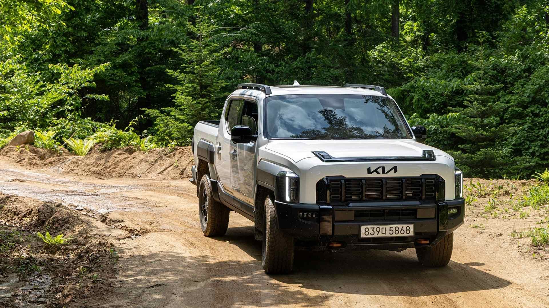 White Kia pickup truck driving on a dirt road surrounded by trees