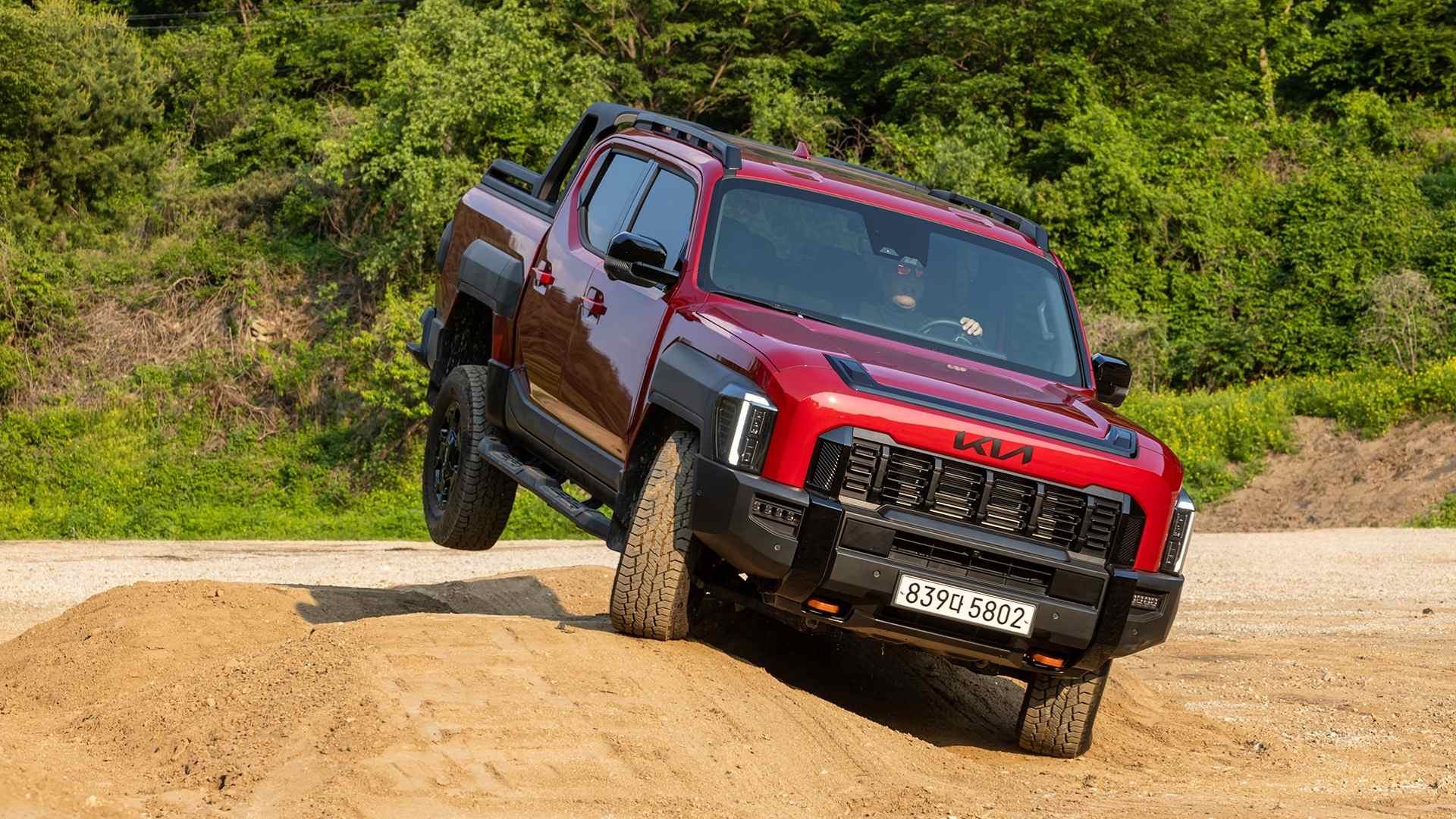Red Kia pickup truck driving over a dirt mound with one wheel lifted off the ground