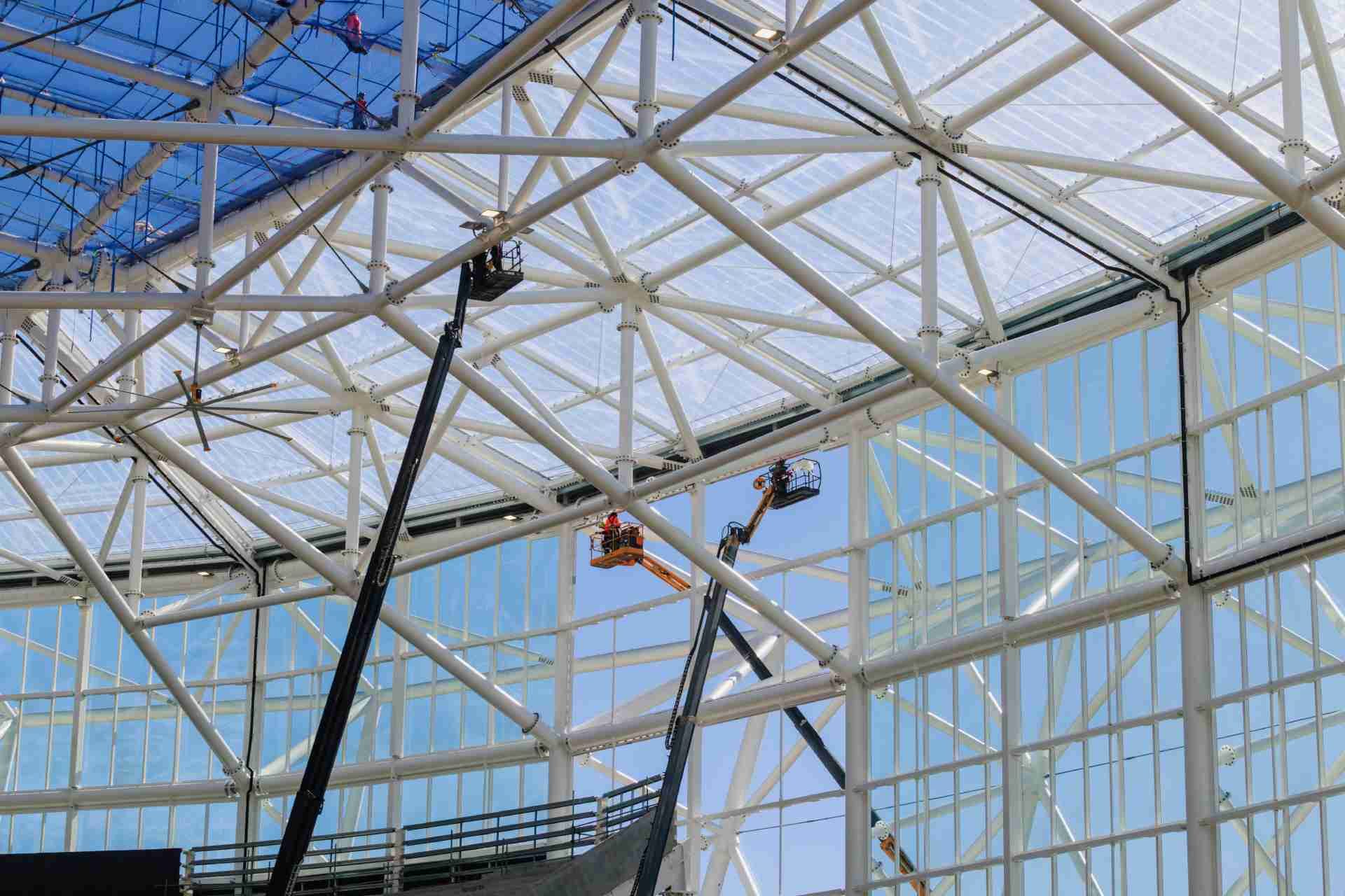 Interior stadium roof structure with workers on elevated lifts installing panels and framework